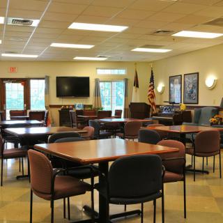 A spacious meeting room with multiple tables, chairs, a TV, and flags.