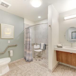 A modern and accessible bathroom featuring a shower, toilet, and sink with a light color scheme.