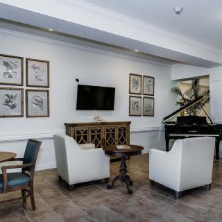 A stylish living room featuring white armchairs, a piano, wall art, and a television.