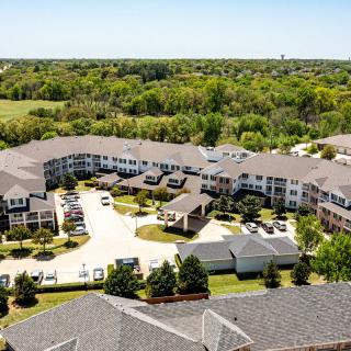 Aerial view of a suburban apartment complex surrounded by greenery and featuring a central parking area.