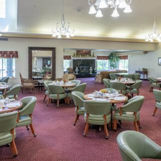 A spacious dining room with round tables set for a meal, featuring elegant chandeliers and green chairs on a red carpet.