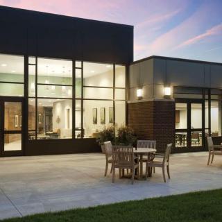 A modern building with a spacious patio area, featuring outdoor furniture and evening lighting.