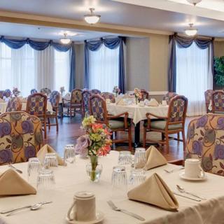A well-decorated dining area with neatly arranged tables and chairs, featuring folded napkins and floral centerpieces.