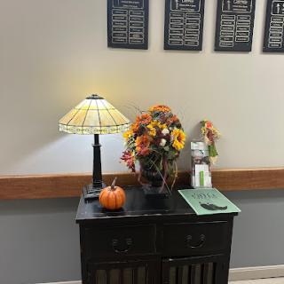 A cozy corner with seasonal decor featuring a lamp, autumn flowers, and a small pumpkin.