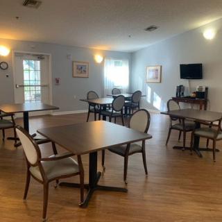 An empty dining room with tables and chairs, featuring bright lighting and a television on the wall.
