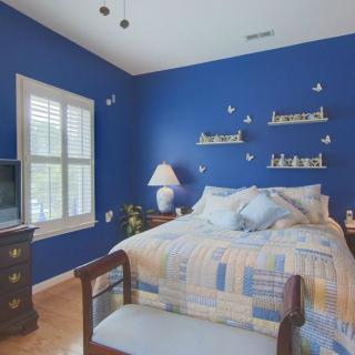 A cozy bedroom with blue walls, featuring a bed and decorative shelves.