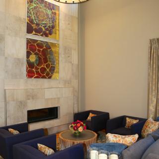 A modern living room with blue armchairs, a fireplace, and abstract artwork.