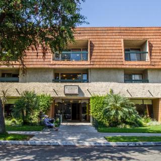 A multi-story building with a brick facade and a lush green entrance.