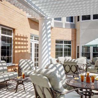A sunny outdoor patio with comfortable seating and tables under a pergola.