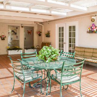 A sunlit patio with a glass table and chairs, adorned with plants and decorative items.