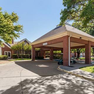 A building entrance with a covered driveway surrounded by trees on a sunny day.