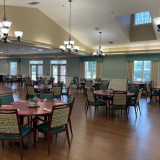 A spacious and elegant dining room with multiple tables and chairs, featuring chandeliers and wooden flooring.