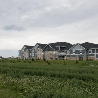 A row of residential buildings set against a cloudy sky with grassy fields in the foreground.