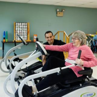 An elderly woman engaging in physical therapy with the assistance of a trainer, using exercise equipment.