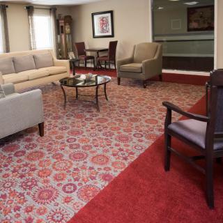 A cozy lounge area with a patterned carpet, multiple chairs, and a sofa arranged around a glass coffee table.