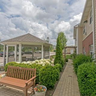 A serene garden pathway with a bench and gazebo under a cloudy sky.