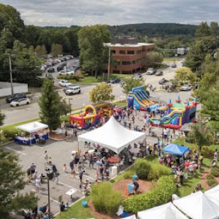 A bustling outdoor community event featuring various attractions, including bouncy castles and food tents.