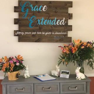 A decorative table setup with floral arrangements and a wooden sign that reads 'Grace Extended'.