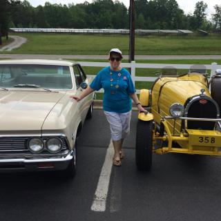 A woman stands between a classic and a vintage car parked outdoors.