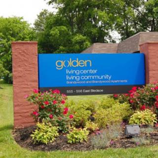 A sign for Golden Living Center, a living community, surrounded by well-maintained gardens and flowers.