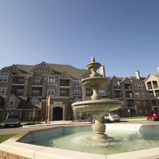 A luxurious apartment complex with a prominent fountain in the foreground on a clear day.
