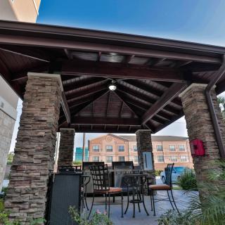 An outdoor gazebo with stone pillars and patio furniture, providing a shaded seating area.