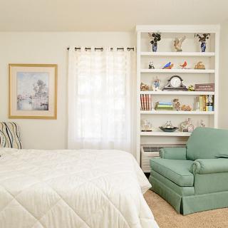 A cozy bedroom with a white bookshelf and a green armchair.