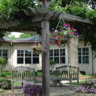 A serene garden setting featuring a pergola adorned with hanging flowers and comfortable seating.