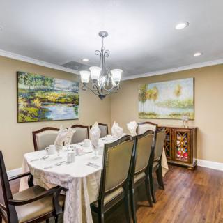 A well-decorated dining room with a chandelier, artwork on the walls, and a set dining table.