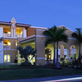 An illuminated residential building with palm trees at night.