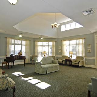 A spacious living room with ample natural light, featuring comfortable seating and a piano.