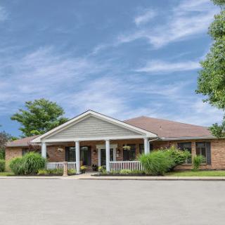 A welcoming single-story residential building surrounded by lush greenery and a clear blue sky.