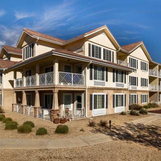 A large two-story residential building with a wraparound porch in a sunny landscape.