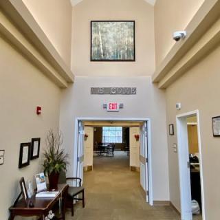 A well-lit office hallway featuring artwork, a bench, and a plant arrangement.