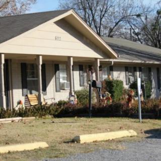 A suburban house with a porch, surrounded by trees and a driveway.