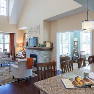 A modern open-concept living room and kitchen with a cozy fireplace and high ceilings, featuring large windows that bring in natural light.