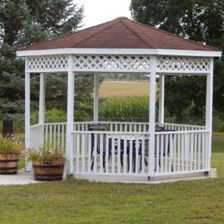 A white wooden gazebo in a garden setting surrounded by greenery.