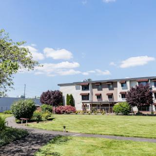 A serene view of a residential building surrounded by lush greenery under a clear blue sky.