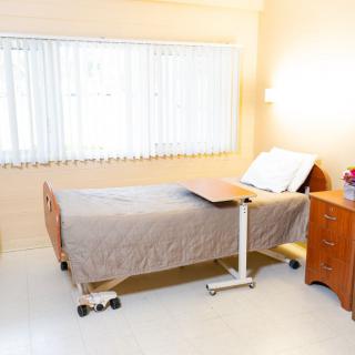 A clean and well-lit hospital room with a single bed and bedside furniture.