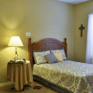 A cozy bedroom with a wooden bed frame, patterned bedspread, and a lamp on the nightstand.