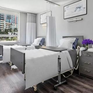 A modern hospital room with two neatly made beds and bright natural lighting.