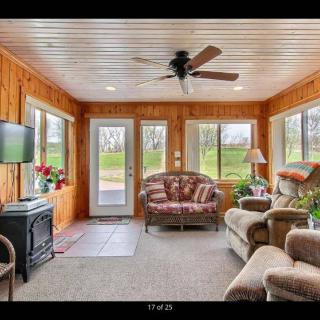 A cozy sunroom with wood paneling, featuring comfortable furniture, a ceiling fan, and large windows offering a view of the outdoors.