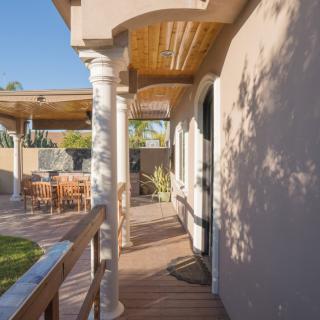 A sunny outdoor patio with a wooden deck, columns, and seating area.