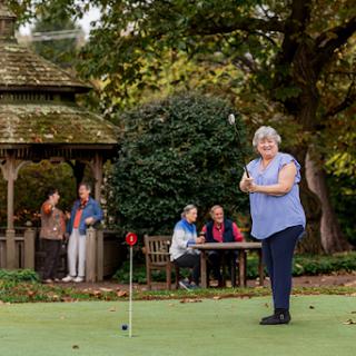 A group of seniors enjoys a day of golfing and socializing in a beautiful garden setting.