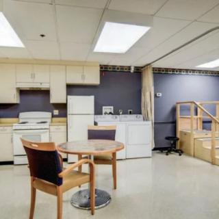 A kitchen area with appliances, a table, and chairs in a well-lit room.