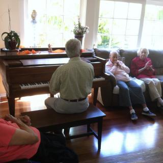 A person playing piano in a living room while others are seated and listening.