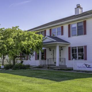 A two-story house with a well-maintained front yard and trees on a sunny day.