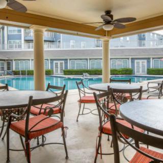 A covered patio with tables and chairs overlooks a swimming pool.