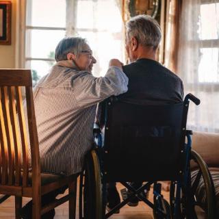 Two elderly individuals sitting together, one in a wheelchair, sharing a moment of companionship by the window.