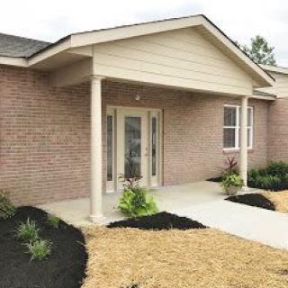 A brick house with a front entrance featuring columns and landscaping.